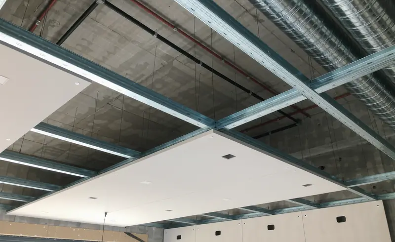 Falso techo en obra con estructura metálica vista, conductos de ventilación y placas de pladur ya colocadas